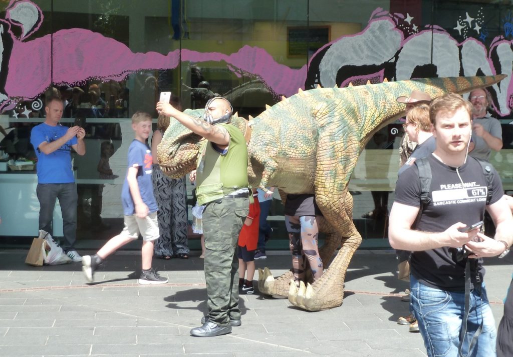 A dinosaur having it's photo taken by a masked man